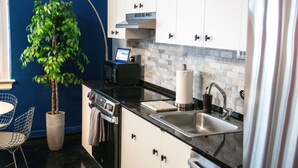 A modern kitchen with white cabinets, a black countertop, a built-in microwave, a stainless steel sink, and a potted plant. - Modern 1BR Downtown condo with rooftop gym & skyline views. King bed, Wi-Fi, walk to Canal & FQ (New Orleans)