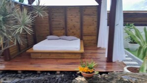 Una terraza de madera con una cama, una pequeña planta en maceta y una fuente de agua.