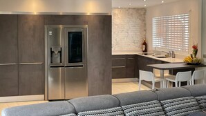 Una cocina moderna con refrigerador integrado, un comedor con sillas blancas y un sofá gris.