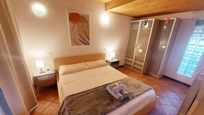 Hotellihuone, jossa on sänky, yöpöytä, lamppu, vaatekaappi ja ikkuna, josta on näkymä.