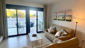 Un salon comprenant un canapé, une table basse et une lampe. Une porte-fenêtre coulissante donne sur un espace extérieur aménagé avec une table et des chaises.
