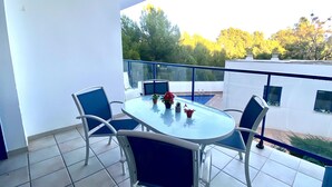 Un balcon avec une table et des chaises en verre, une petite piscine et une vue sur les arbres et les bâtiments.