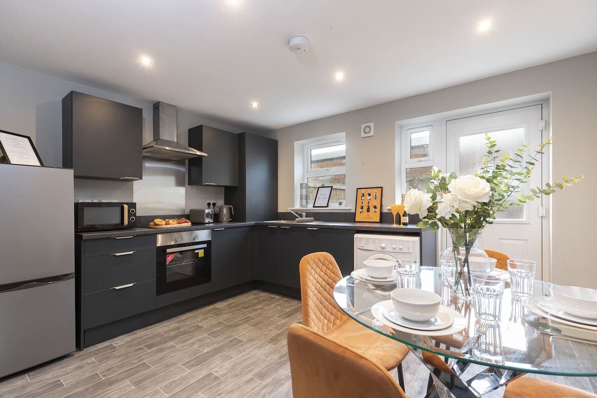 A modern kitchen with dark cabinetry, a glass dining table, and a vase with flowers.