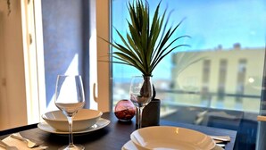 Ein Esstisch mit Tellern, Gläsern und Besteck, einer Topfpflanze und Blick auf Gebäude durch ein Fenster.