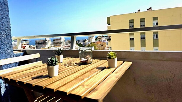 Ein Holztisch mit Blumentöpfen auf einem Balkon mit Blick auf eine Stadtlandschaft und das Meer.