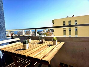 Una mesa de madera con plantas en macetas en un balcón con vistas a un paisaje urbano y al mar.