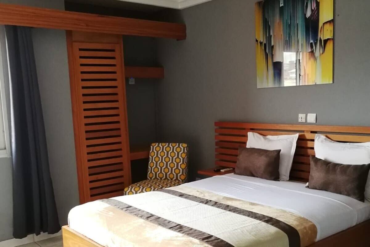 A modern hotel room with a wooden bed, a patterned armchair, and a large abstract painting on the wall.