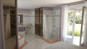 Une chambre avec un grand lit, un dressing, une douche et une porte-fenêtre coulissante donnant sur l’extérieur.