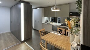 Eine moderne Küche mit Essbereich, ausgestattet mit einem Holztisch und Stühlen, einer Pendelleuchte und einem eingebauten Backofen.