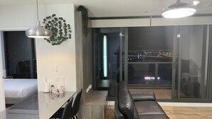 Ein modernes Wohnzimmer mit Essbereich, großen Fenstern und Blick auf die Stadt sowie einer schwarzen Ledersofa.