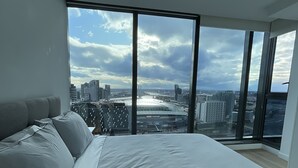 Ein Schlafzimmer mit einem großen Bett, Blick auf eine Stadtlandschaft und modernem Design.