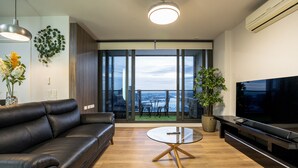 Ein modernes Wohnzimmer mit Ledersofa, Glastisch, Flachbildfernseher und einem Balkon mit Stadtblick.