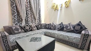 Ein Wohnzimmer mit einem Ecksofa, gemusterten Kissen, einem sofaähnlichen Möbelstück mit Marmoroptik und einem Couchtisch mit Marmorplatte.