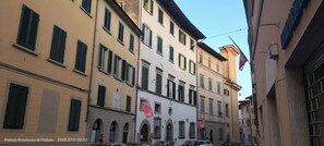 A narrow street with historic buildings, some with visible signage and flags.