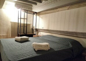 A hotel room with a bed, a radiator, and a window with curtains.