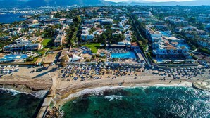 An aerial view of a coastal resort with multiple swimming pools, a beach area with sun loungers, and a marina. - Annabelle Beach Resort (Hersonnisos, Crete)