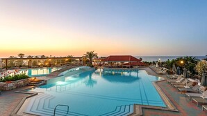 A large outdoor swimming pool with a red-roofed building in the background, surrounded by lounge chairs and umbrellas. - Annabelle Beach Resort (Hersonnisos, Crete)