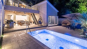 Et moderne hus med swimmingpool, udendørs møbler og spiseområde.
