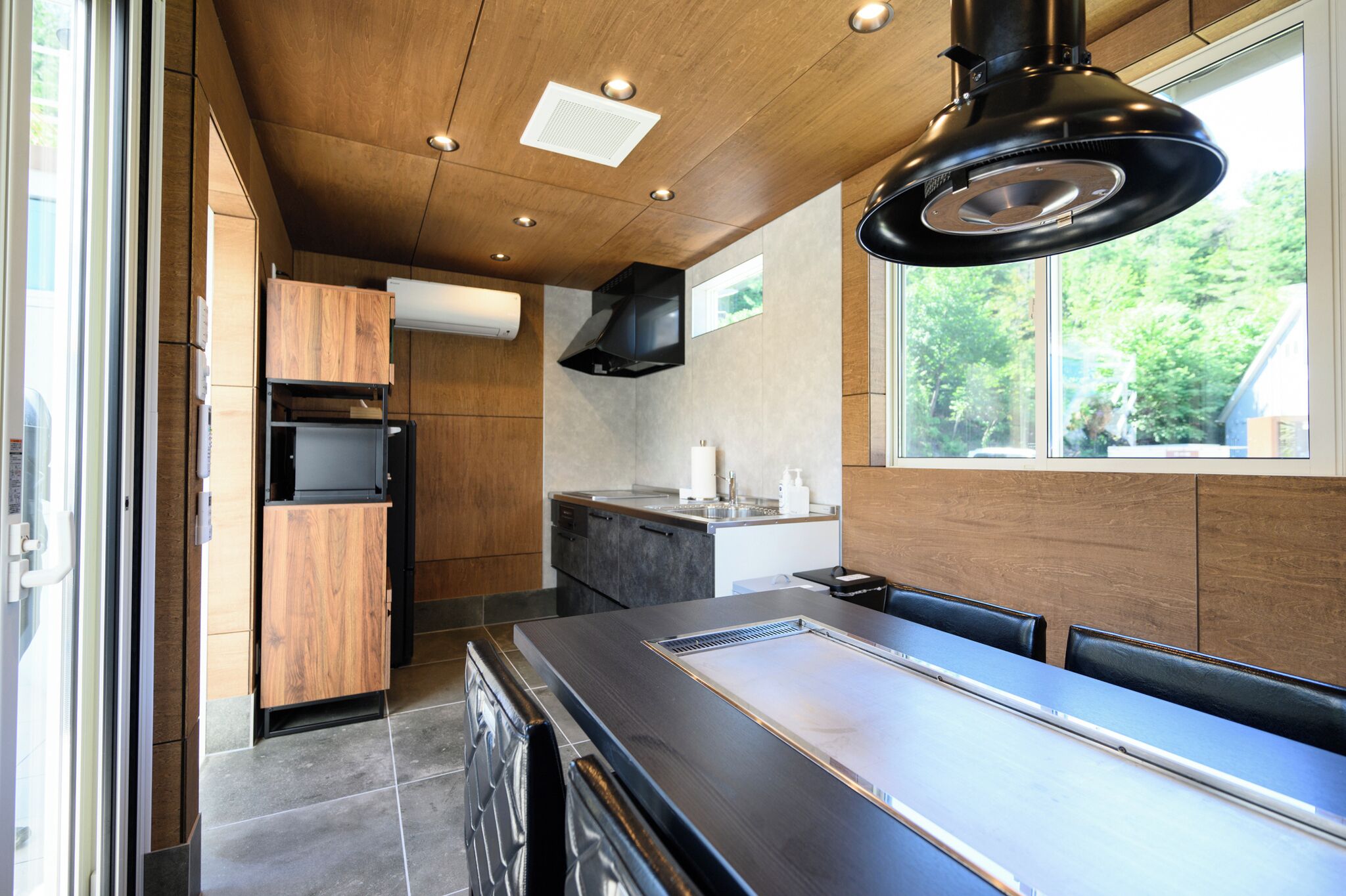 A modern kitchen with wooden cabinets, a black countertop, and a window with a view of greenery.