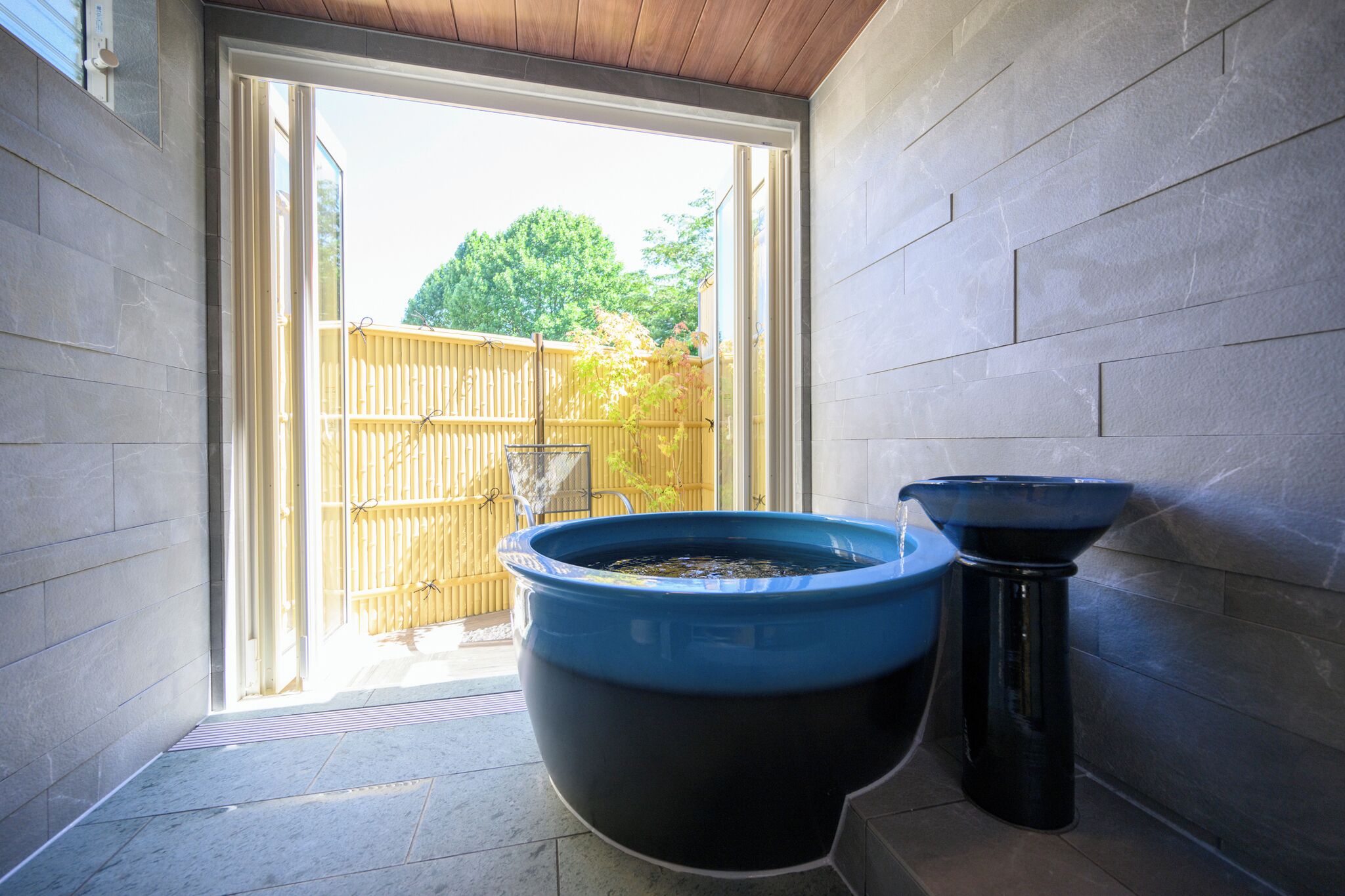 Un baño con una bañera grande de color negro y azul, un lavamanos pequeño y una cerca de madera visible a través de la puerta.