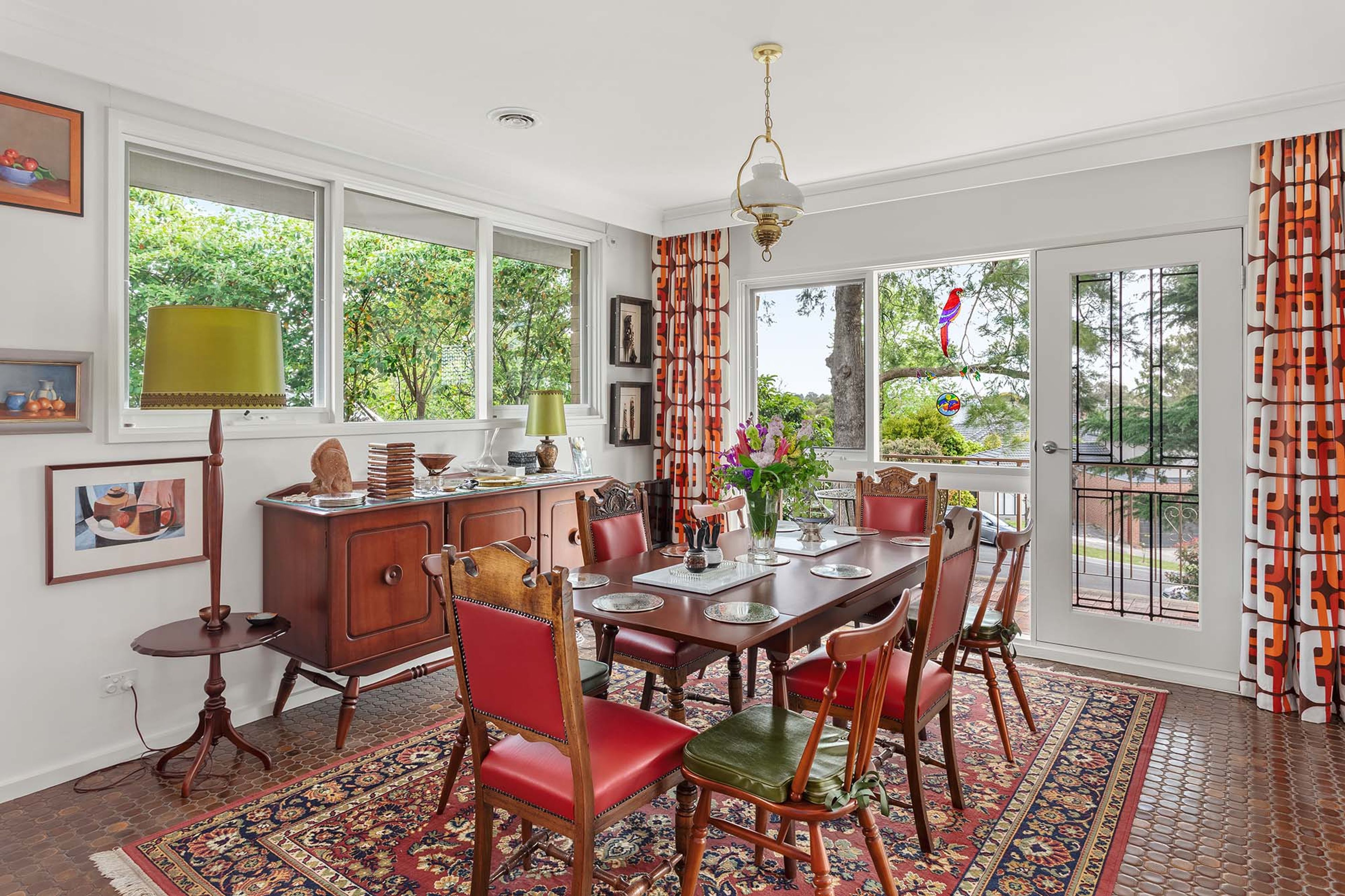 A dining room with a large table, chairs, a chandelier, and a view of greenery outside.