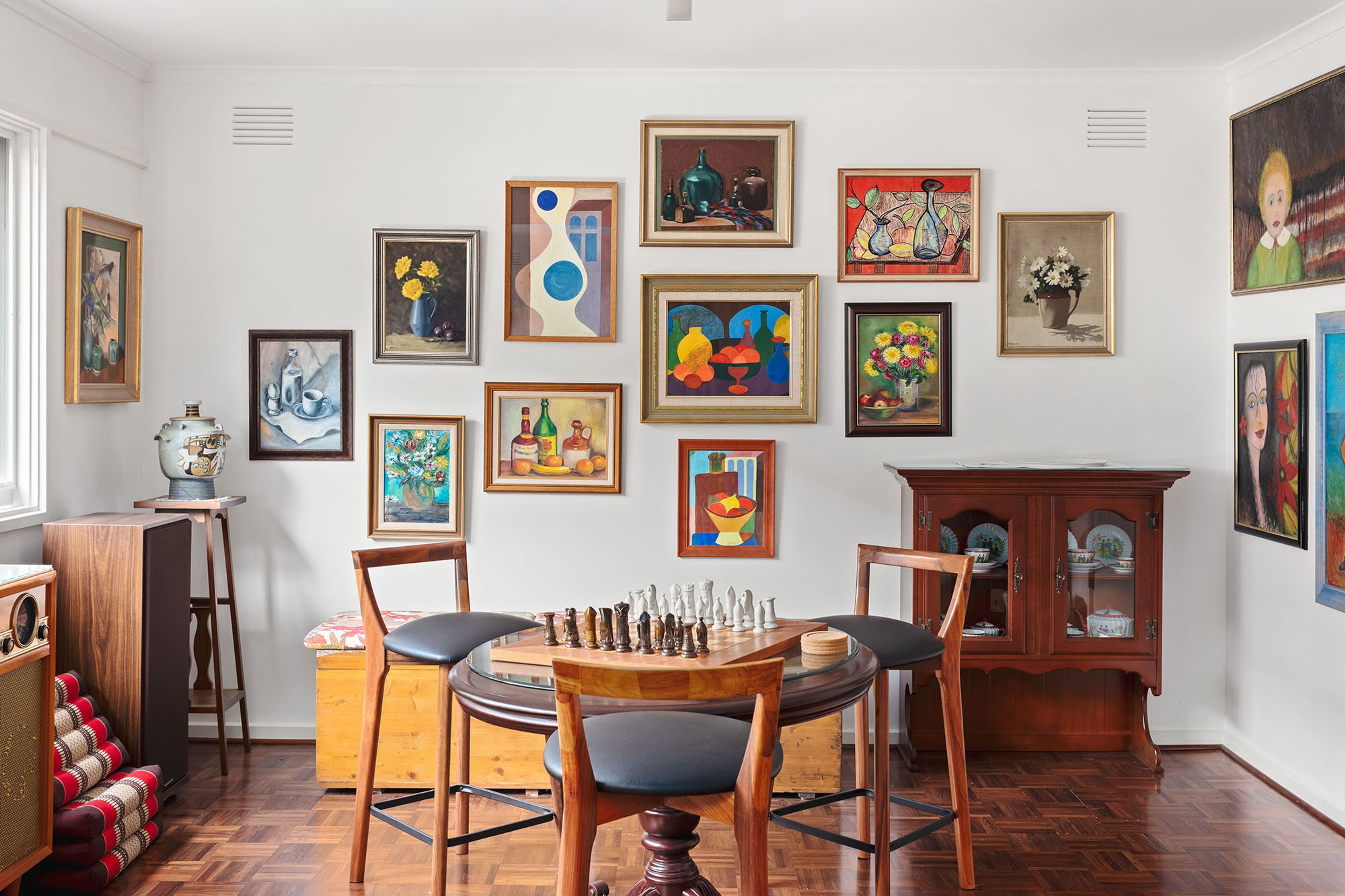 Ein Zimmer mit Schachbrett, Stühlen, einem Schrank und verschiedenen gerahmten Kunstwerken an der Wand.