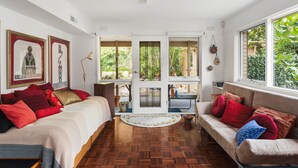 A room with a wooden floor, a sofa, a bed, and a window with a view of greenery. - That 70s House in Mount Waverley (Mount Waverley)