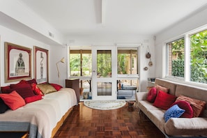 A room with a wooden floor, a sofa, a bed, and a window with a view of greenery. - That 70s House in Mount Waverley (Mount Waverley)