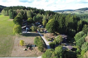 A rural property with multiple buildings, a paved driveway, and surrounding forested hills.