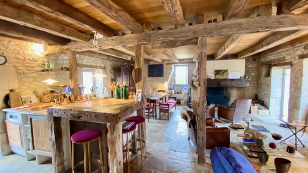 Un interior rústico con vigas de madera a la vista, una pared de piedra y una zona de bar con taburetes.