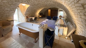 Habitación de paredes de piedra con una bañera, una cama, un escritorio y una silla.