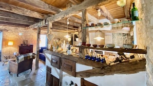 Un interior rústico con vigas de madera a la vista, paredes de piedra y una encimera de madera con diversos utensilios de cocina.
