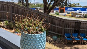 A potted plant on a wooden deck with a view of a fenced area and a building in the background. - Cute, cozy country escape in a new unit close to cherry and strawberry orchards (Maddingley)