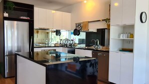 A modern kitchen with white cabinetry, a central island, and a built-in oven. - Cute, cozy country escape in a new unit close to cherry and strawberry orchards (Maddingley)