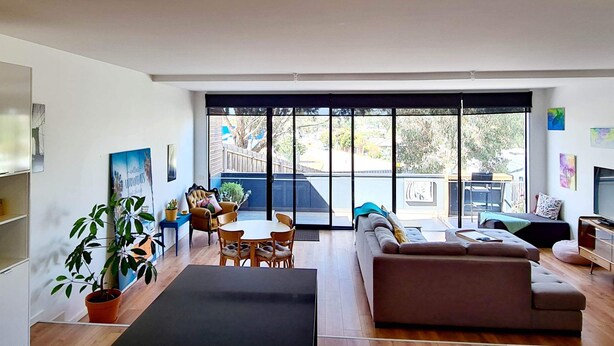 A modern living room with a sofa, dining table, chairs, and a large window. - Cute, cozy country escape in a new unit close to cherry and strawberry orchards (Maddingley)
