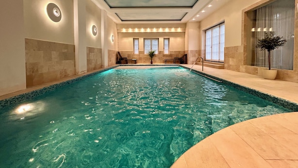 Ein großer, überdachter Swimmingpool mit klarem Wasser, umgeben von Wänden mit integrierter Beleuchtung und einem mit Oberlichtern versehenen Deckenbereich.