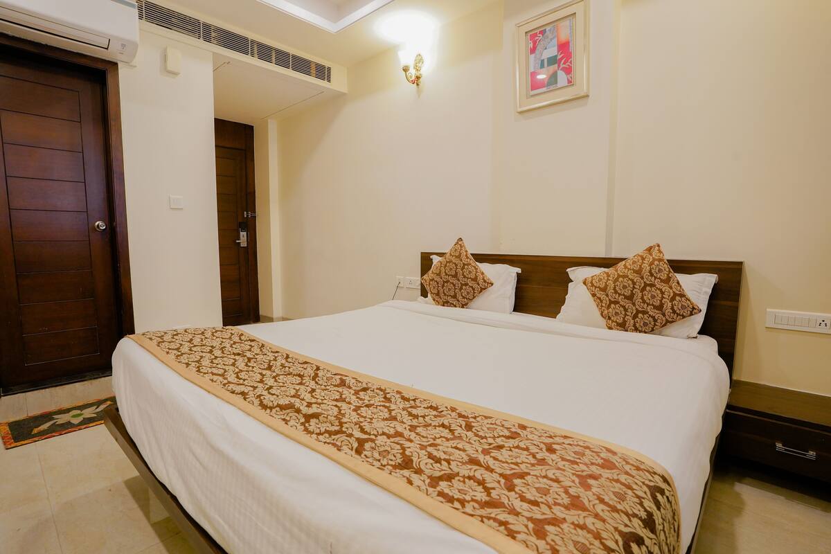 Habitación de hotel con cama, puerta de madera, equipo de aire acondicionado, lámpara fijada a la pared y un cuadro enmarco.