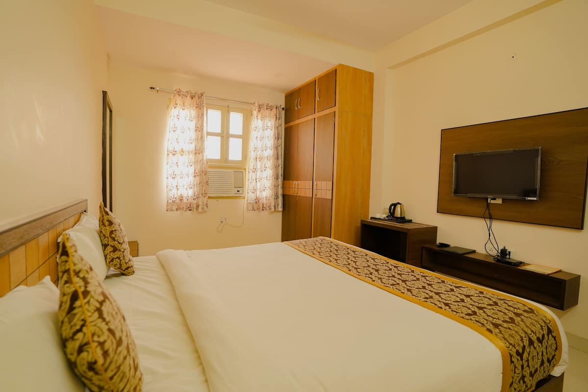 Habitación de hotel con una cama grande, un armario de madera, un televisor montado en la pared y una ventana con cortinas florales.