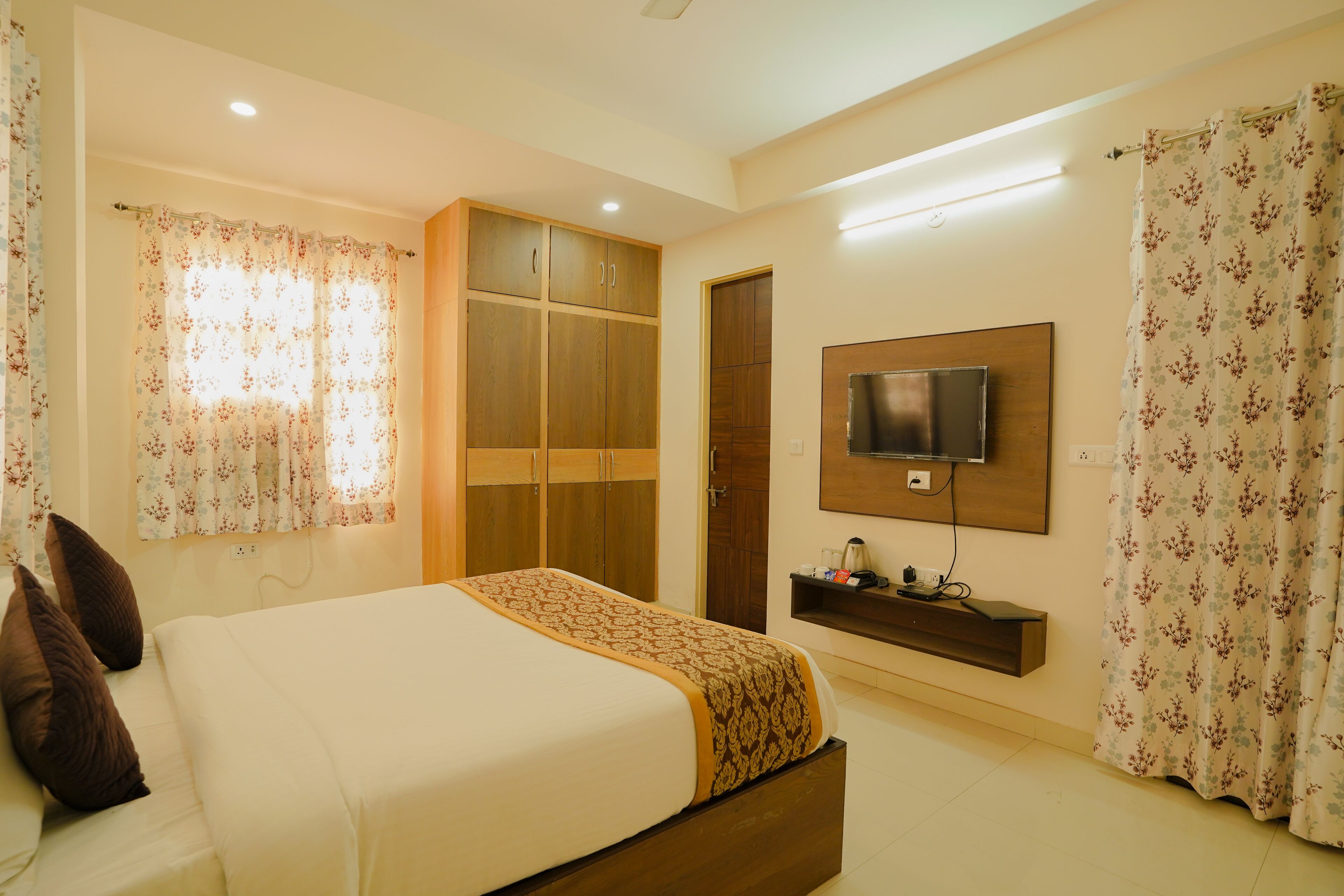 A bedroom with a bed, wooden wardrobe, TV, and curtains.