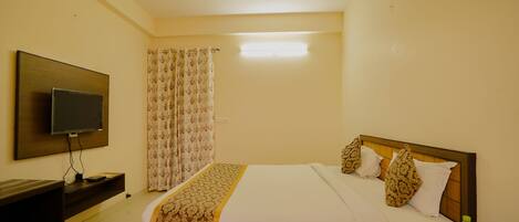 Habitación de hotel con cama, televisor, ventilador de techo y mesita de noche con botellas de agua.