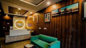 A reception area with a wooden wall, a reception desk, a green sofa, and framed pictures. - Hotel Cheelgadi (Jaipur)