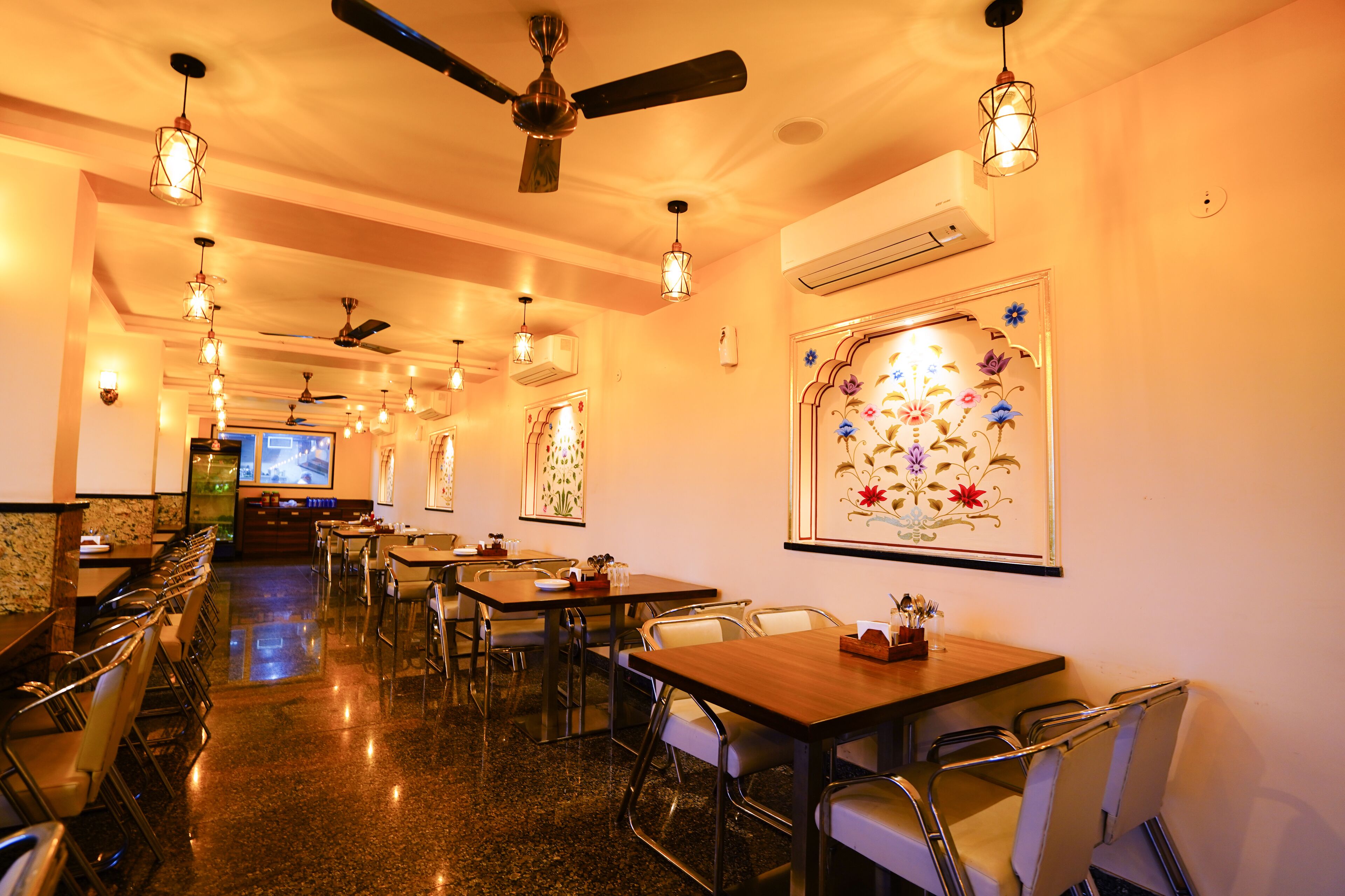 Un restaurante con varias mesas y sillas, ventiladores de techo y lámparas colgantes.