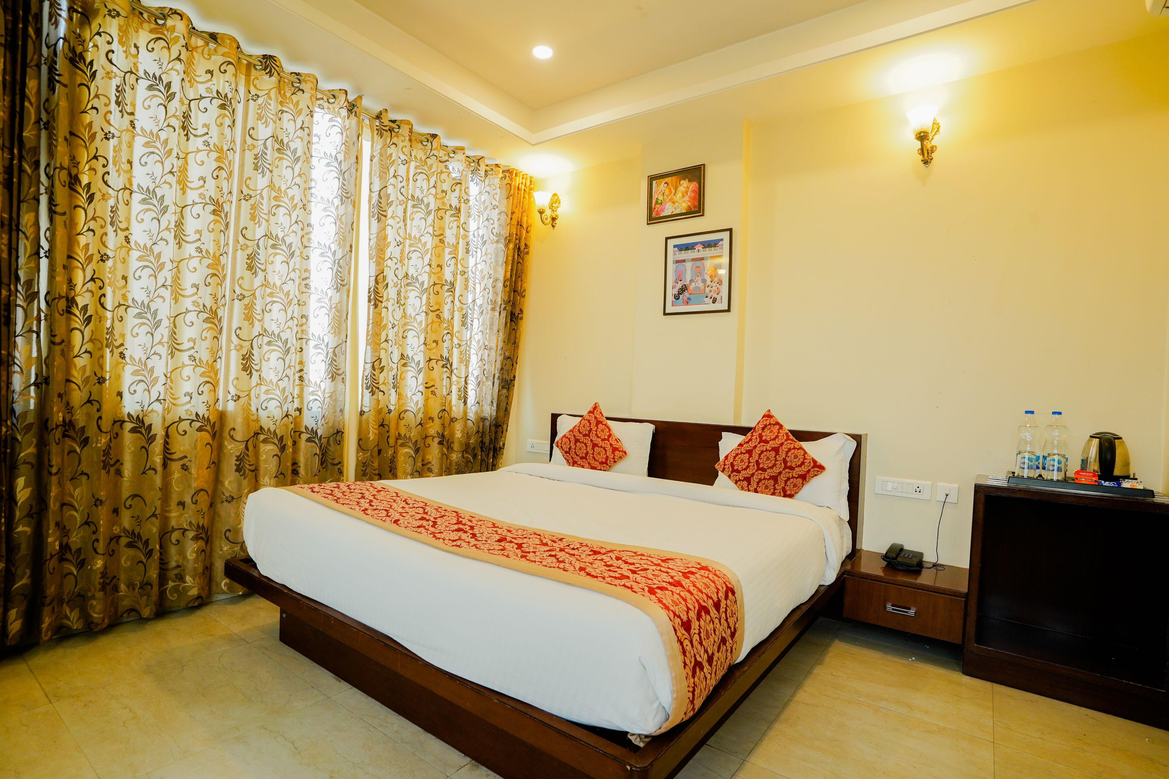 A hotel room with a large bed, curtains, a bedside table with a lamp, and a wall-mounted picture.