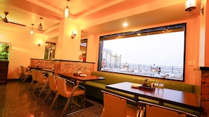 A restaurant with a view of a balcony and a large window. There are tables and chairs arranged for dining. - Hotel Cheelgadi (Jaipur)