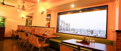 A restaurant with a view of a balcony and a large window. There are tables and chairs arranged for dining.