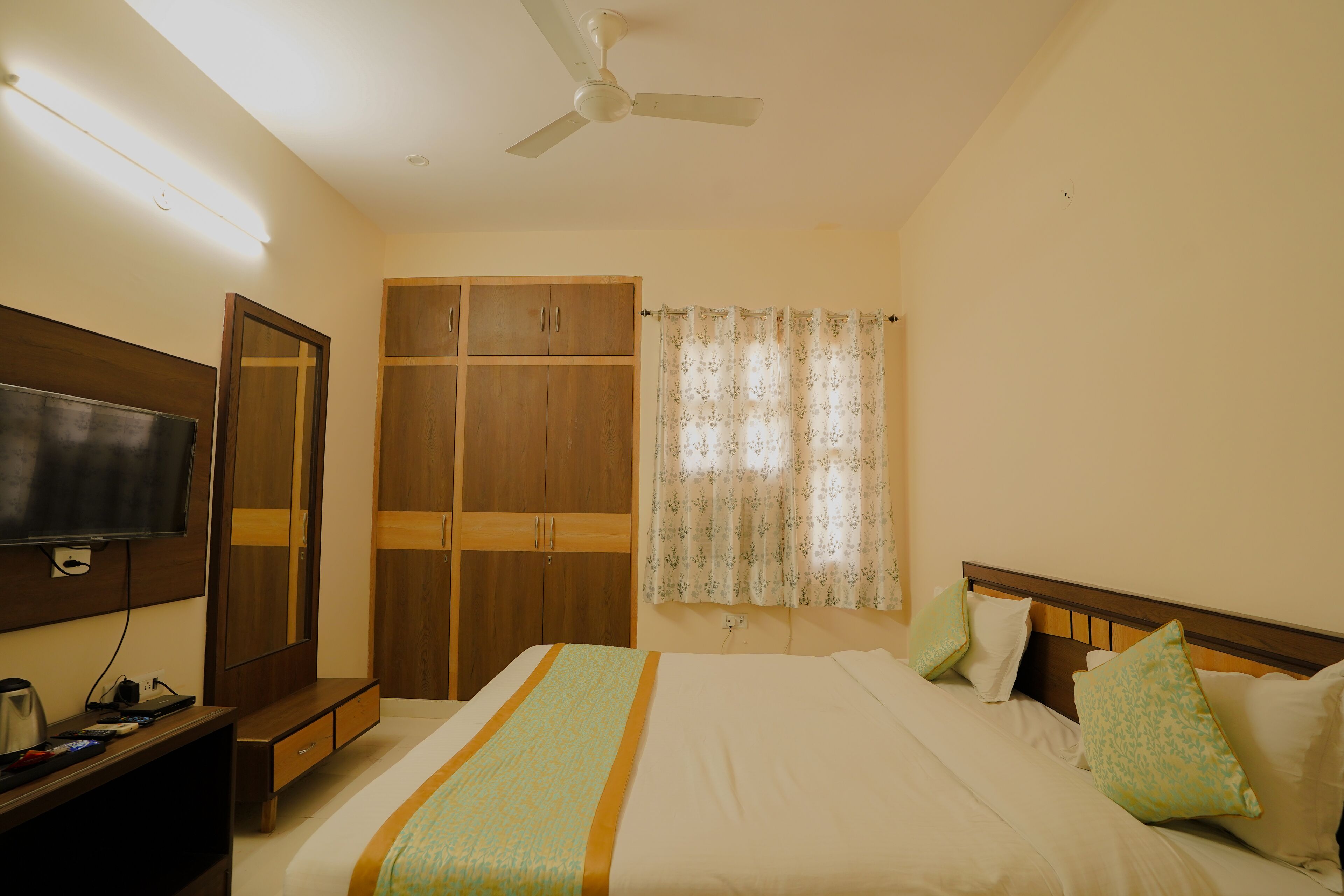 A hotel room with a bed, a TV, a wardrobe, and a ceiling fan.