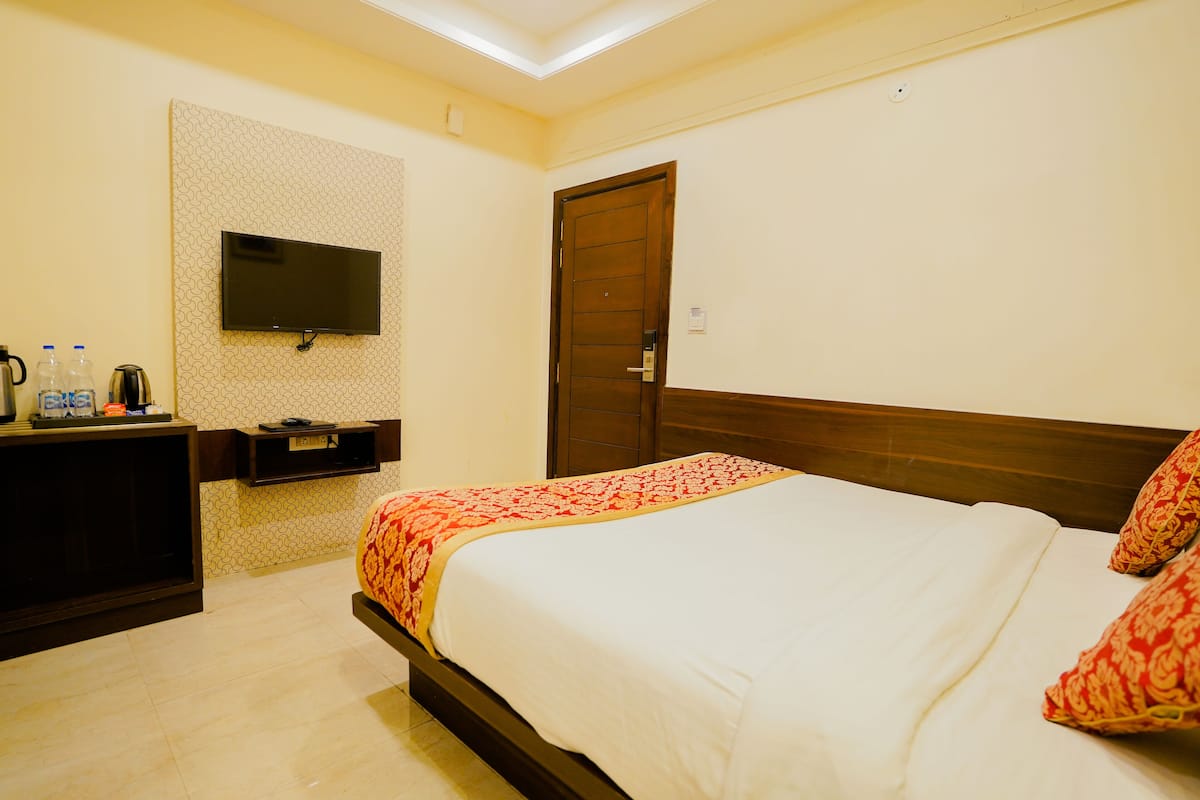 Habitación de hotel con cama, televisor montado en la pared, puerta de madera y un estante con objetos.