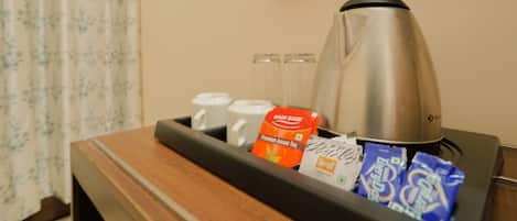 A tray with a stainless steel coffee pot, two white mugs, a packet of premium Assam tea, and several packets of instant coffee.