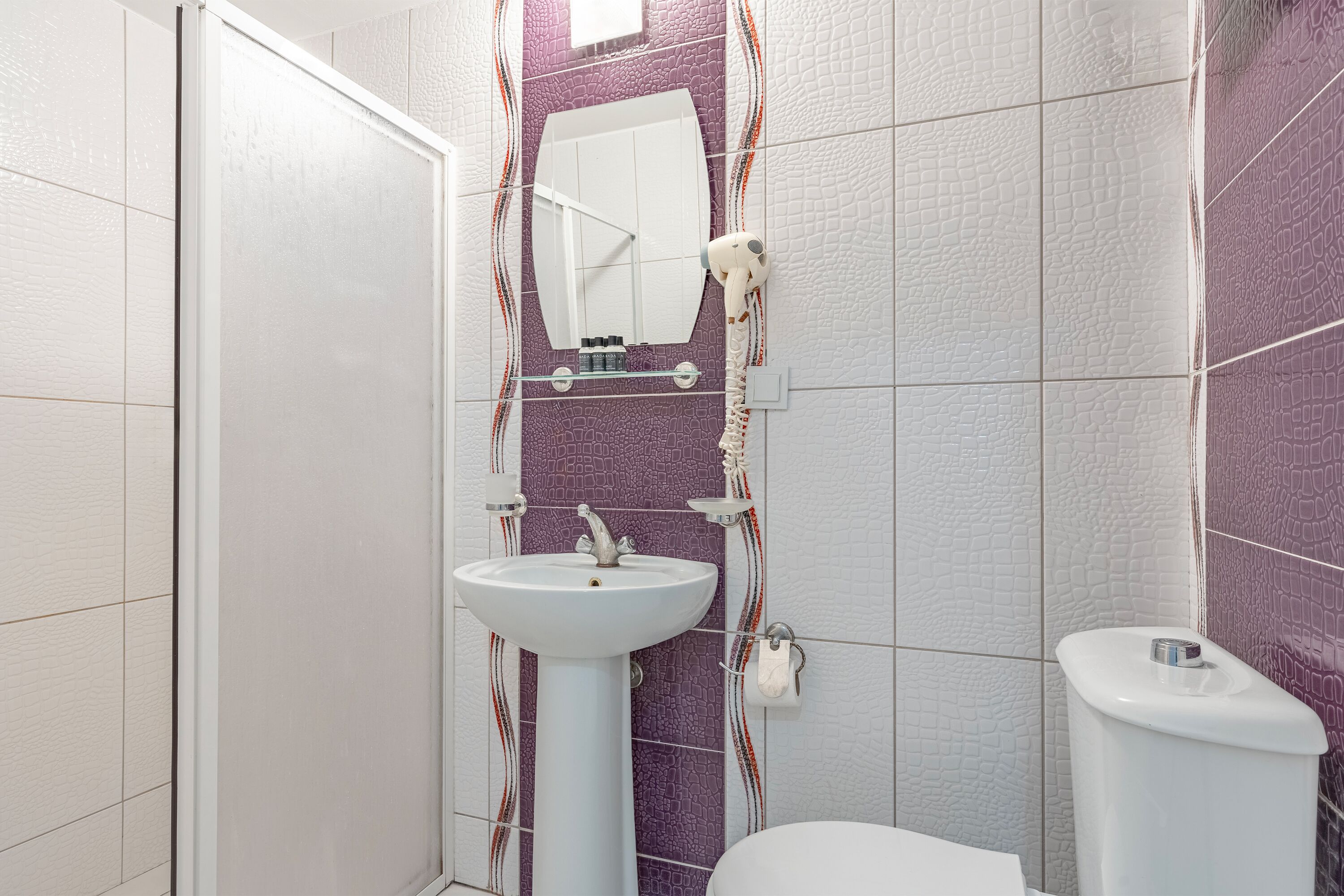 A bathroom with a pedestal sink, a mirror, a toilet, and a shower area.