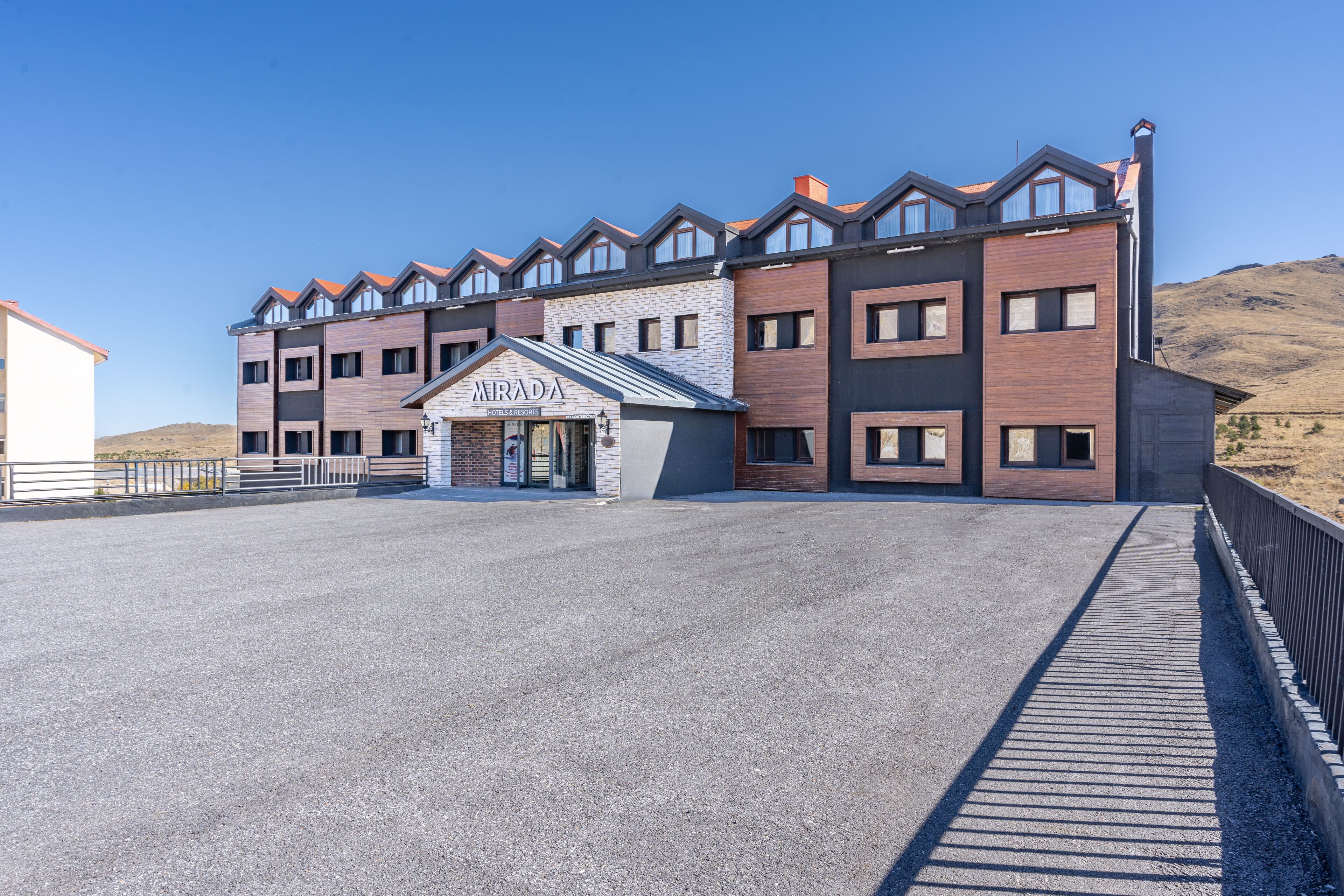 A modern hotel with a prominent 'Mirada' sign, featuring a mix of brick and wood facade, multiple balconies, and a spacious entrance area.